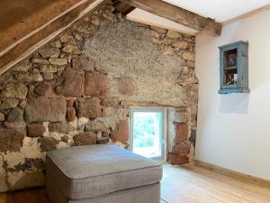 a room with a stone wall with a couch and a window at La Belle Petite Ferme Rosiers de Julliac 19350 in Les Bos