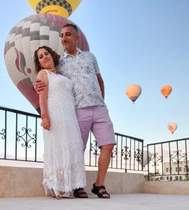 a man and woman standing next to a fence with hot air balloons at Cappadocia Fairy Tale Suites in Çavuşin