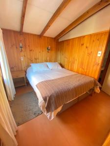 Cama grande en habitación con paredes de madera en Torres Del Sur Cabañas & Hostal, en Villarrica