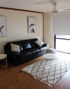 a living room with a black leather couch and a table at Investigator Beach Breeze Apartments U2 in Kingscote