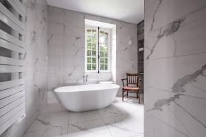La salle de bains blanche est pourvue d'une baignoire et d'une fenêtre. dans l'établissement Au vieux Château, à Villotran