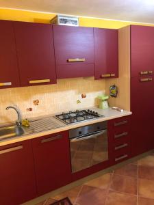 La cuisine est équipée de placards rouges et d'un four avec plaques de cuisson. dans l'établissement Basicò un balcone sul mare - Casa SALITA FOTI -Case vacanza Sicilia&Toscana-, à Basicò
