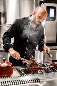 a man in a kitchen preparing food in a pan at Rossano Boutique Hotel & Ristorante in Ansbach