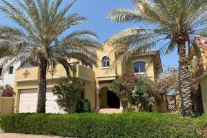 a large yellow house with palm trees in front of it at Villa Quinta on Palm Jumeirah - 5 BR + kids room in Dubai