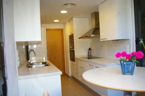 una cocina con armarios blancos y flores rosas en un jarrón en Apartamento PR 39 terraza y piscina Tossa de Mar, en Tossa de Mar