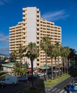 a tall building with palm trees in front of a parking lot at Apartamentos Teneguia in Puerto de la Cruz