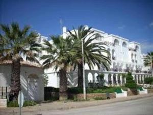 a large white house with palm trees in front of it at Tavira Small cozy flat by the pool and by the sea in Tavira