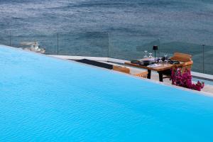 a swimming pool with a table and chairs next to the ocean at Panormos Village Hotel in Mykonos