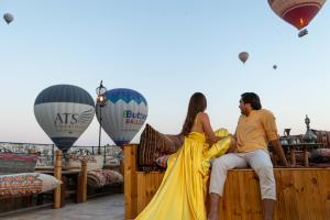 a man and woman sitting on a fence with hot air balloons at Helen Cave Suites in Goreme