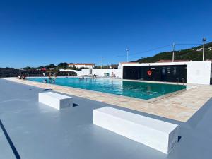 a swimming pool with two white benches in front of it at Casa da Abrótea in Lajes do Pico