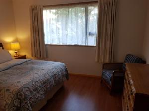 a bedroom with a bed and a window and a chair at Wakari Holiday Home in Dunedin
