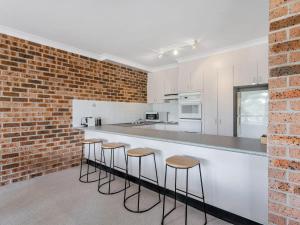 a kitchen with white cabinets and a brick wall at Cottage Court 4 Shoal Bay and Little Beach at your fingertips in Nelson Bay