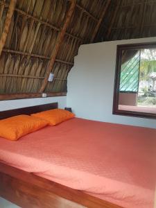 a bed with an orange pillow and a window at Mi Casa en la Playa in Escuintla