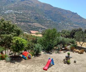 a playground with a slide in the sand with a mountain at levante studios Αndros in Ménites