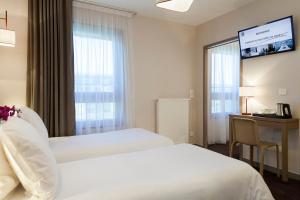 a hotel room with two beds and a desk and a window at Nehô Suites Porte de Genève in Annemasse