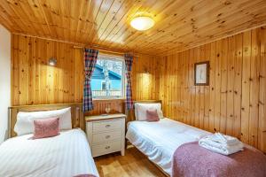 two beds in a room with wooden walls at Bracken Lodge 6 with Hot Tub in Belladrum