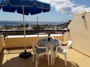 una mesa y sillas en un balcón con sombrilla en MIRAMAR ATTICO, en Morro del Jable