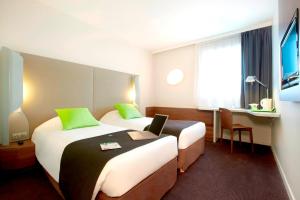 a hotel room with two beds and a desk with a laptop at Campanile Montbéliard - Sochaux in Sochaux