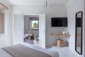 a white bedroom with a bed and a tv at Ammothines Cycladic Suites in Naxos Chora