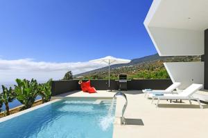 a swimming pool with two chairs and an umbrella at Villa Crow in Tijarafe