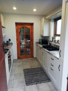 a kitchen with white cabinets and a sink and a door at Craig Cottage Self-catering in Bushmills