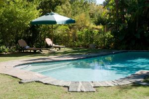 a swimming pool with an umbrella and a bench and a table at Willowbrook Country House in Somerset West