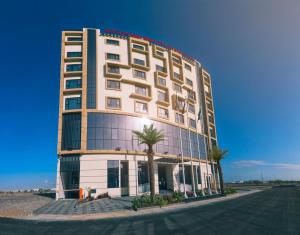 een hoog gebouw met palmbomen ervoor bij Boulevard Hotel Oman in Seeb