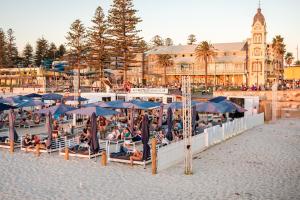 a group of people sitting under umbrellas on the beach at Beachside Luxury Apartments One & Two Bedroom in Beachfront Oaks Pier Building in Glenelg