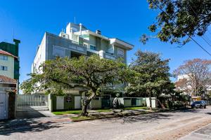 a tall white building with a tree in front of it at Apto 2 Suites, Ideal Para famílias, 30m do mar in Florianópolis