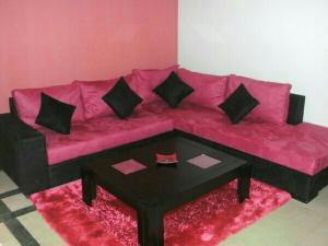 Sofá rosa con almohadas negras y mesa de centro en résidence les jardins, en El Aouina