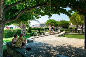 two women sitting on a park bench under a tree at Apartments and Room Mate-Mare in Primošten