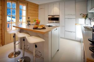 una cocina con armarios blancos y una isla con taburetes. en Chalet Le Mousqueton - OVO Network, en La Clusaz