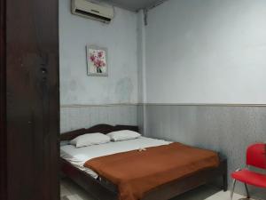 Cama pequeña en habitación con silla roja en OYO 90529 Hotel Baruga Makassar, en Makassar