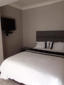 The Eden Lodge Boksburg في بوكسبرغ: غرفة نوم مع سرير أبيض كبير مع تلفزيون بشاشة مسطحة