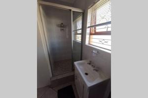 a white bathroom with a sink and a shower at Cozy, peaceful garden cottage in Cape Town