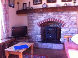 sala de estar con chimenea de piedra y TV en The Stables - 200 Year Old Stone Built Cottage en Foxford