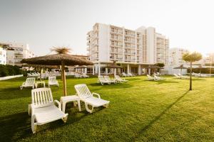 a group of white chairs and an umbrella in a field at Hotel Gran Sol in San Antonio