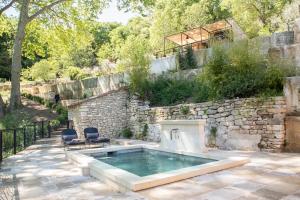 een zwembad met 2 stoelen naast een stenen muur bij Les Cabanes de la Fontaine in Lacoste
