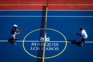 two men standing on a tennis court holding rackets at Marquis Los Cabos, an All - Inclusive, Adults - Only & No Timeshare Resort in San José del Cabo