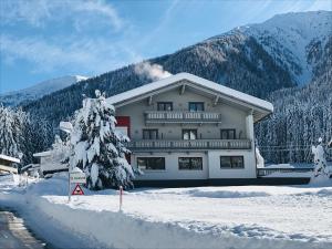 un grand bâtiment dans la neige devant une montagne dans l'établissement Hotel Garni Burger, à Sankt Jakob in Defereggen