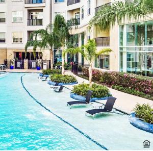 a pool with chairs and palm trees in front of a building at Corporate rental unit City Centre, Energy Corridor in Houston