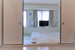 a white bed sitting in a room next to a television at U-Community Hotel in Osaka