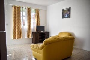 un salon avec un canapé jaune et une télévision dans l'établissement Green Castle Apartment#3 in City of Roseau, à Roseau
