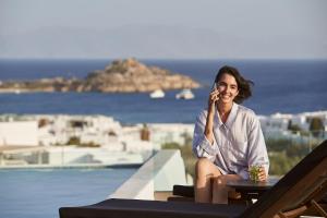 a woman sitting at a table talking on a cell phone at Mr & Mrs White Mykonos in Platis Gialos