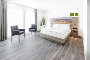 a white bedroom with a bed and two chairs at Landhotel Kirchberg in Kirchberg an der Jagst