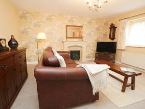 a living room with a leather couch and a fireplace at 3 Springfort Cottages in Penrith