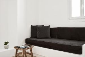 a black couch in a white room with a stool at Mr & Mrs White Mykonos in Platis Gialos