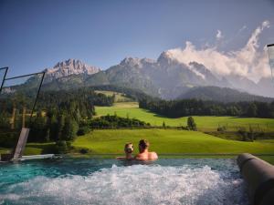 Due persone in una vasca idromassaggio con vista sulle montagne di Hotel Salzburger Hof Leogang a Leogang