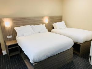 two beds in a hotel room with white sheets at De Regency Style Hotel in Redditch