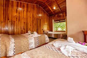 two beds in a room with wooden walls at Cabañas La Pradera in Monteverde Costa Rica +57 photos